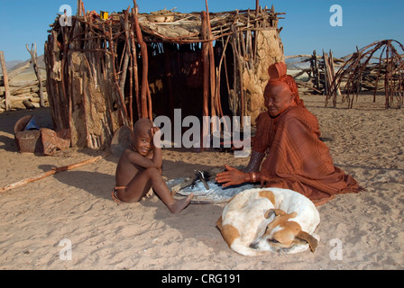 Il villaggio tradizionale di Purros, Himba Donna con bambino e cane nella parte anteriore di una capanna, Namibia, Purros Foto Stock