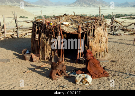 Il villaggio tradizionale di Purros, Himba donna con bambini e cane nella parte anteriore di una capanna, Namibia, Purros Foto Stock