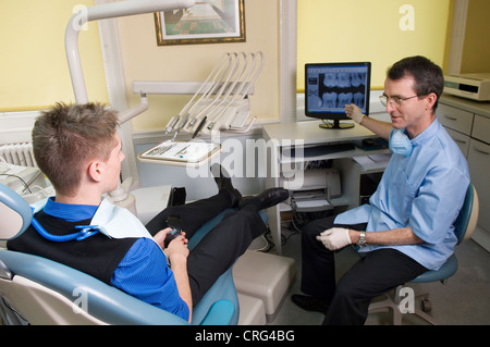 Dentista davanti allo schermo di un computer, illustra i risultati di un esame a raggi x con un giovane paziente di sesso maschile Foto Stock