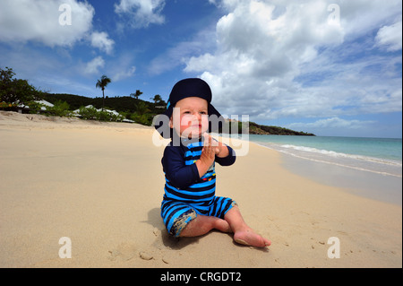 Da un anno un ragazzo che indossa la protezione dal sole abbigliamento, gioca con la sabbia, Grand Anse Beach, Grenada, Caraibi, West Indies Foto Stock