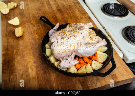 Un pollo crudo preparato per la tostatura con le patate e le carote in una ghisa padella Foto Stock