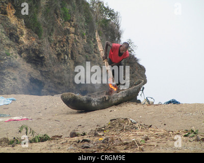 Uomo che ripara il suo fisherboat fatta di un scavato a Mango Tree, verniciatura con tar con una torcia ardente, Haiti, Grande Anse, le albicocche Foto Stock