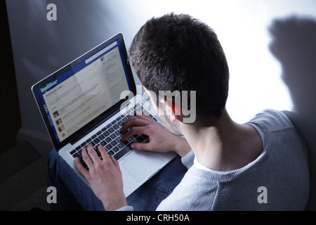 Giovane maschio seduta usando un computer portatile guardando a Twitter Foto Stock
