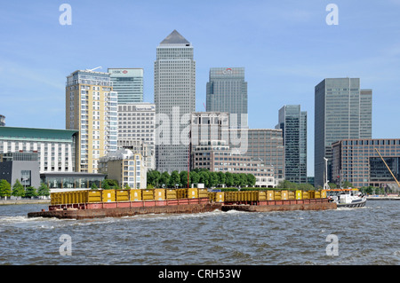 Rimorchiatore con barconi caricati con rifiuti di Londra sul Fiume Tamigi con alta marea passando Docklands di Londra Canary Wharf skyline Foto Stock