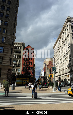 Sunny nuvole grigie ritratto, verso West 23rd Street, donna tirando caso attraversando Broadway a East 23rd Street, New York Foto Stock