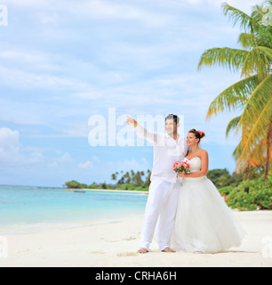 Una sposa tenendo un mazzo di fiori e lo sposo guardando verso, girato su una spiaggia di Isola di Kuredu, Maldive, Lhaviyani atoll Foto Stock
