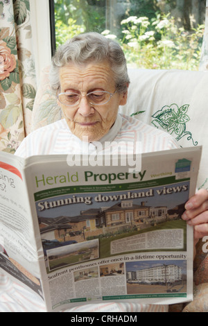 Donna anziana guardando le proprietà sulla pagine delle proprietà in un giornale locale Foto Stock