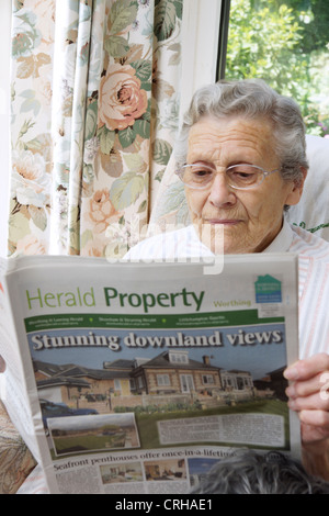 Donna anziana guardando le proprietà sulla pagine delle proprietà in un giornale locale Foto Stock