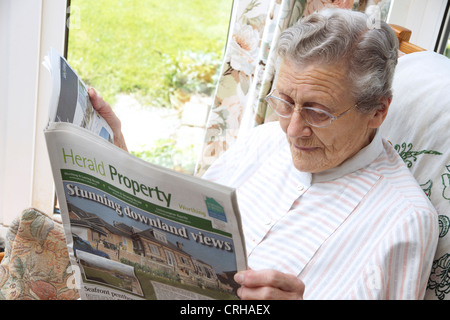 Donna anziana guardando le proprietà sulla pagine delle proprietà in un giornale locale Foto Stock