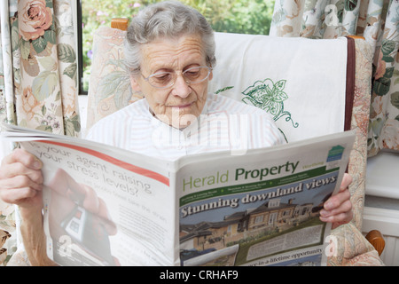 Donna anziana guardando le proprietà sulla pagine delle proprietà in un giornale locale Foto Stock