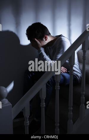 Giovane uomo seduto su per le scale e la sua mano che copre il volto. Foto Stock