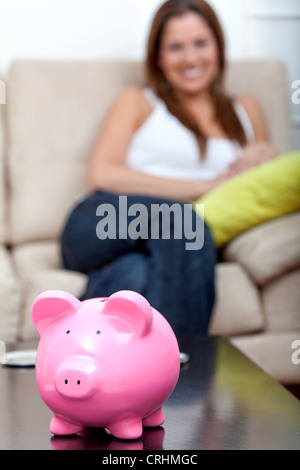 Rosa piggybank in piedi di fronte a una donna seduta su un divano dietro Foto Stock