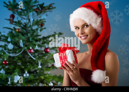 Donna che indossa Santa hat e tenendo presente il Natale, ritratto Foto Stock