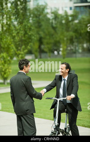 Saluto gli imprenditori a vicenda con handshake, un uomo in bicicletta Foto Stock