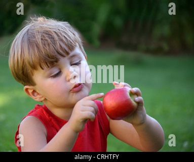 Piccolo Ragazzo con una mela rossa, seduti in un prato Foto Stock