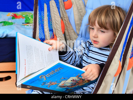 Little Boy in pigiama la lettura di un libro per bambini sui pirati in una oscillazione di un Billi-Bolli loft bed Foto Stock