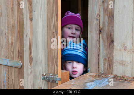 Due bambini curiosi con bobble caps, guardando attraverso una porta, Germania Foto Stock