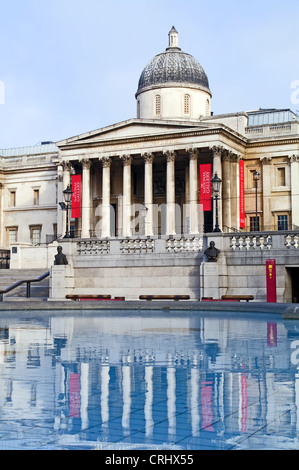 Vista frontale della National Gallery di Londra, riflessa nell'acqua ancora di una piscina con fontana, Trafalgar Square, la mattina presto. Foto Stock