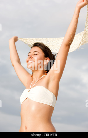 Felice giovane donna in bikini in spiaggia e godersi il sole con le braccia tese Foto Stock