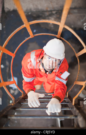 Lavoratore scaletta di arrampicata alla raffineria di petrolio Foto Stock