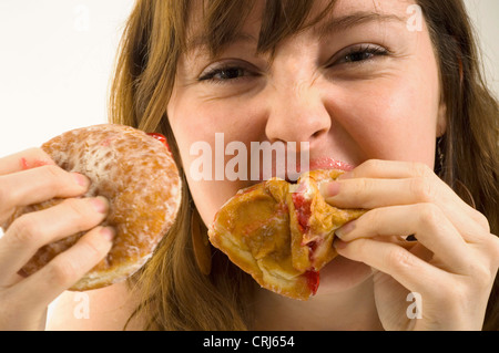 Un giovane femmina imbottisce la sua bocca piena di ciambelle con marmellata. Jam Donut hanno criticato dal cibo spazzatura gli attivisti in guerra globale sull'obesità come insalubre con scarso valore nutrizionale. Il termine "junk food" è stato coniato da Michael Jacobson, Direttore del Centro per la scienza nel pubblico interesse, per descrivere il cibo che conteneva contengono livelli elevati di grassi saturi, Foto Stock