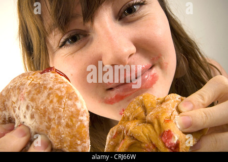 Un giovane femmina imbottisce la sua bocca piena di ciambelle con marmellata. Jam Donut hanno criticato dal cibo spazzatura gli attivisti in guerra globale sull'obesità come insalubre con scarso valore nutrizionale. Il termine "junk food" è stato coniato da Michael Jacobson, Direttore del Centro per la scienza nel pubblico interesse, per descrivere il cibo che conteneva contengono livelli elevati di grassi saturi, Foto Stock