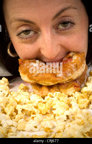 Una giovane donna jam donut junkie con un mucchio di popcorn a seguire. Alimenti come ciambelle con marmellata e pop-corn hanno criticato dal cibo spazzatura gli attivisti in guerra globale sull'obesità come insalubre con scarso valore nutrizionale. Foto Stock