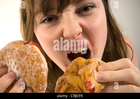 Un giovane femmina imbottisce la sua bocca piena di ciambelle con marmellata. Jam Donut hanno criticato dal cibo spazzatura gli attivisti in guerra globale sull'obesità come insalubre con scarso valore nutrizionale. Il termine "junk food" è stato coniato da Michael Jacobson, Direttore del Centro per la scienza nel pubblico interesse, per descrivere il cibo che conteneva contengono livelli elevati di grassi saturi, Foto Stock