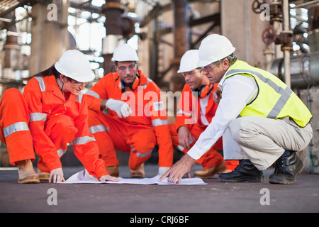 Lavoratori con blueprint alla raffineria di petrolio Foto Stock