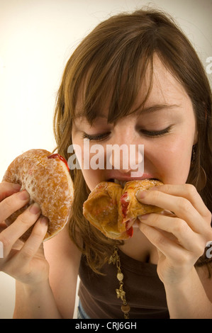 Un giovane femmina imbottisce la sua bocca piena di ciambelle con marmellata. Jam Donut hanno criticato dal cibo spazzatura gli attivisti in guerra globale sull'obesità come insalubre con scarso valore nutrizionale. Il termine "junk food" è stato coniato da Michael Jacobson, Direttore del Centro per la scienza nel pubblico interesse, per descrivere il cibo che conteneva contengono livelli elevati di grassi saturi, Foto Stock