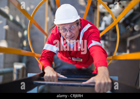 Lavoratore scaletta di arrampicata alla raffineria di petrolio Foto Stock