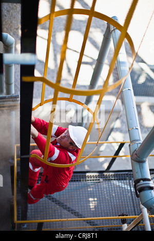 Lavoratore scaletta di arrampicata alla raffineria di petrolio Foto Stock