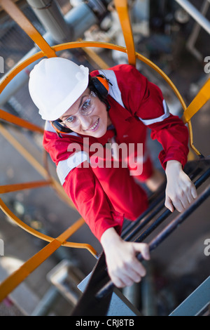 Lavoratore scaletta di arrampicata alla raffineria di petrolio Foto Stock