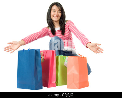 Sorridente ragazza giovane kneeing e presentante quattro borse per lo shopping in piedi di fronte a lei sul terreno Foto Stock