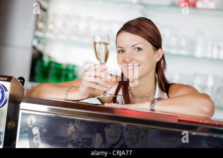 Giovane barista dietro il bar sollevando un bicchiere di vino frizzante con un sorriso Foto Stock