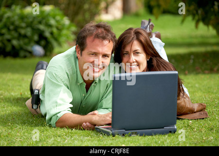 Coppia felice al di fuori con un computer portatile in una giornata di sole guardando molto felici e rilassati - entrambi sorridente Foto Stock