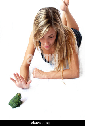 Youn donna sdraiata sul pavimento guardando una rana e non lo vuoi baciare Foto Stock