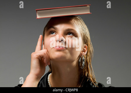 Elegante bionda ragazza di equilibratura di un libro sulla sua testa con indice alzato Foto Stock