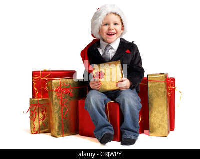 Ragazzo con una Santa cap seduto su una pila di regali di Natale con un sorriso Foto Stock