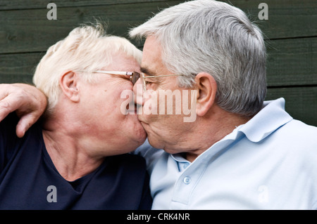 Coppia di anziani su una panchina nel loro giardino kissing Foto Stock