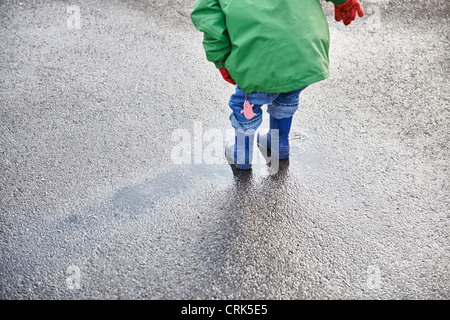 Ragazzo in stivali da pioggia a giocare nella pozza Foto Stock