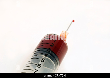 Vista di un ago fissato ad una siringa, la punta dell'ago contiene una gocciolina di liquido. Foto Stock