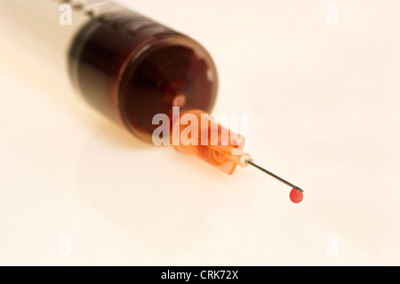 Vista di un ago fissato ad una siringa, la punta dell'ago contiene una gocciolina di liquido. Foto Stock