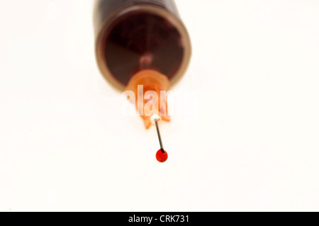 Vista di un ago fissato ad una siringa, la punta dell'ago contiene una gocciolina di liquido. Foto Stock