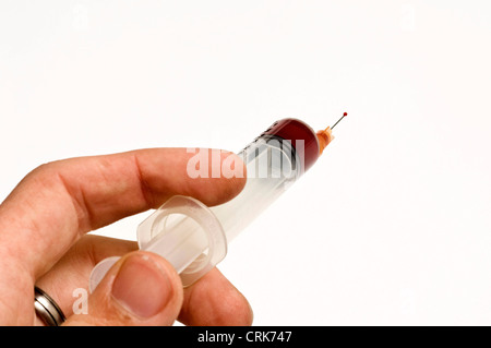 Vista di un ago fissato ad una siringa, la punta dell'ago contiene una gocciolina di liquido. Foto Stock