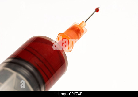 Vista di un ago fissato ad una siringa, la punta dell'ago contiene una gocciolina di liquido. Foto Stock