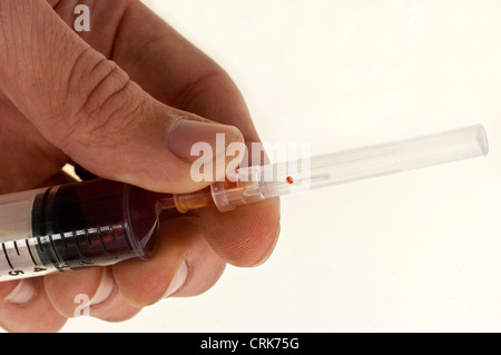 Vista di un ago fissato ad una siringa, la punta dell'ago contiene una gocciolina di liquido. Foto Stock