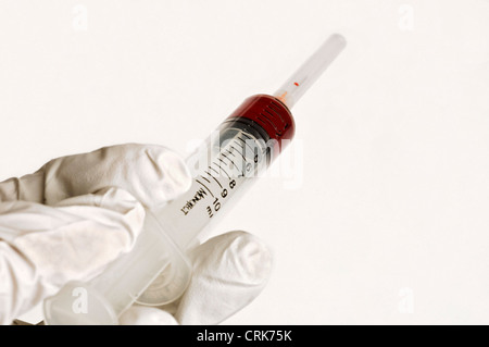 Vista di un ago fissato ad una siringa, la punta dell'ago contiene una gocciolina di liquido. Foto Stock