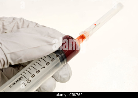 Vista di un ago fissato ad una siringa, la punta dell'ago contiene una gocciolina di sangue. Foto Stock
