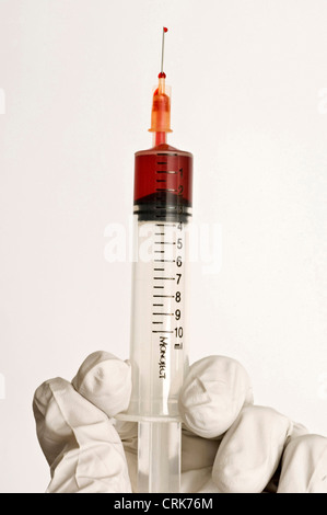 Vista di un ago fissato ad una siringa, la punta dell'ago contiene una gocciolina di liquido. Foto Stock